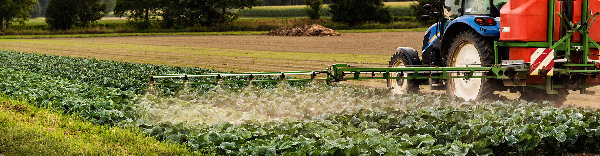 Tractor azul con aspersora AMS trabajando campo de cultivo